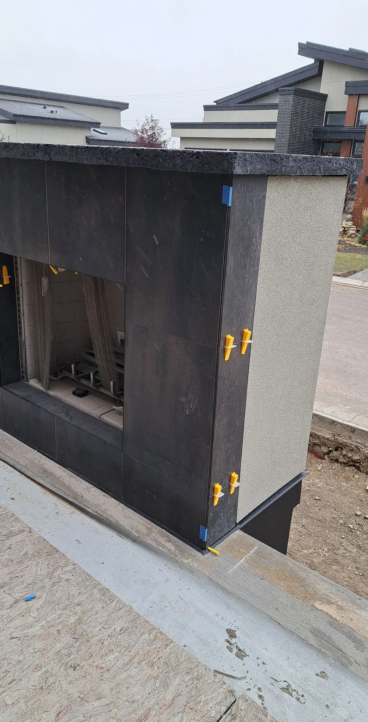 Outdoor fireplace surround clad in dark tile with levelling clips still fitted