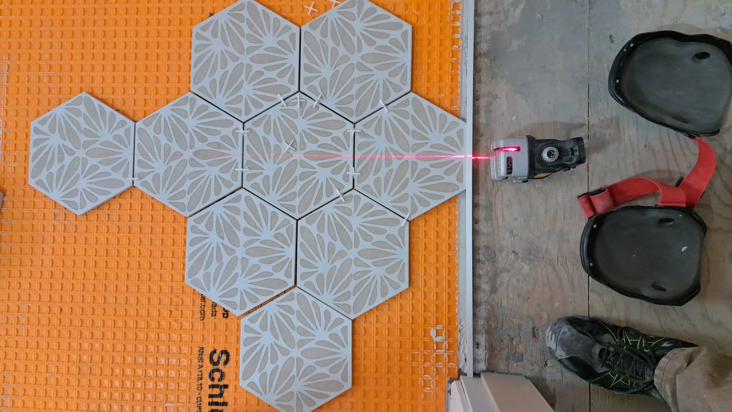 Hexagon tiles being set over an orange uncoupling membrane, laid out against a laser line