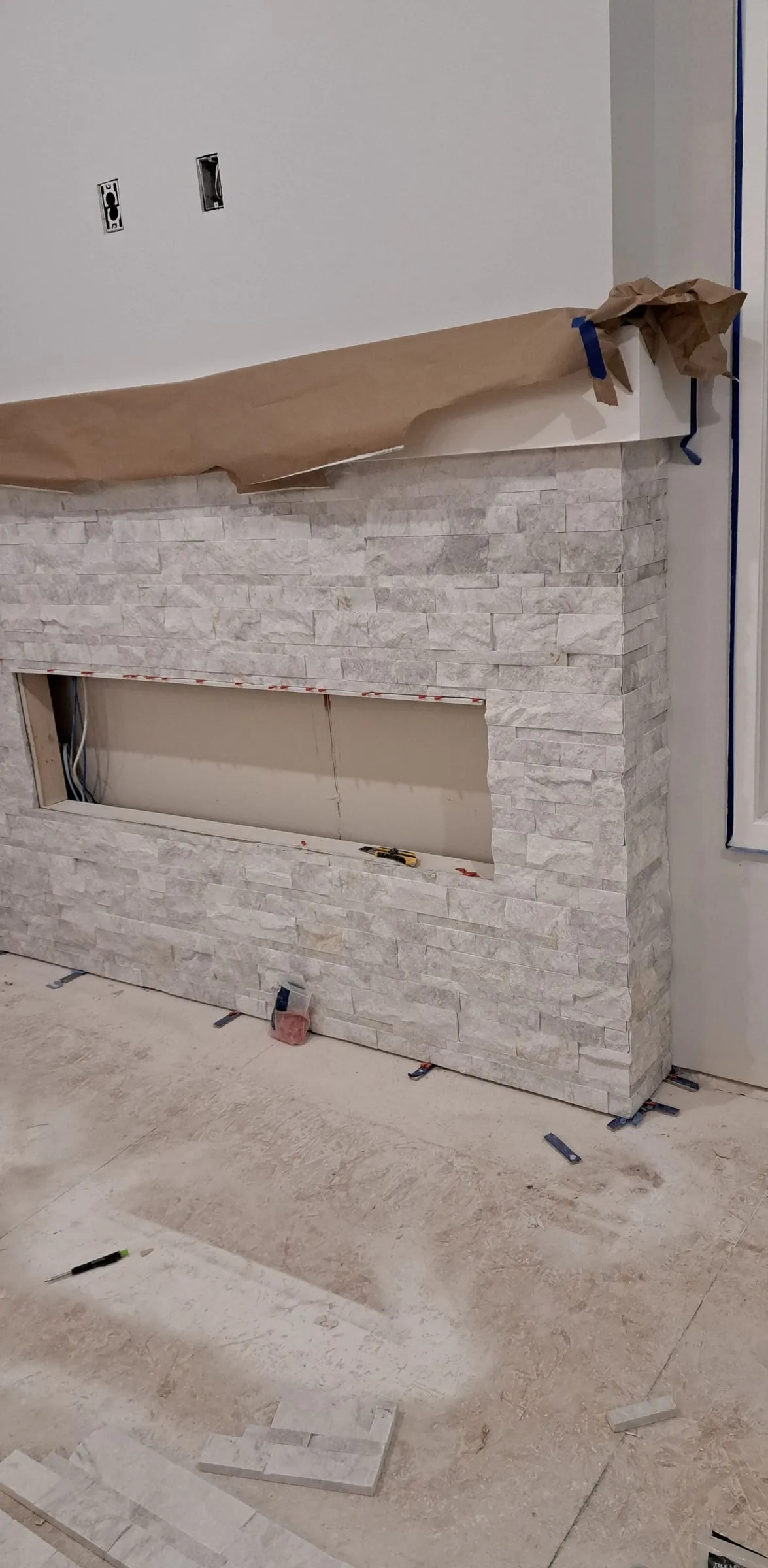 Stone fireplace surround part-built, with the opening framed and the floor still protected
