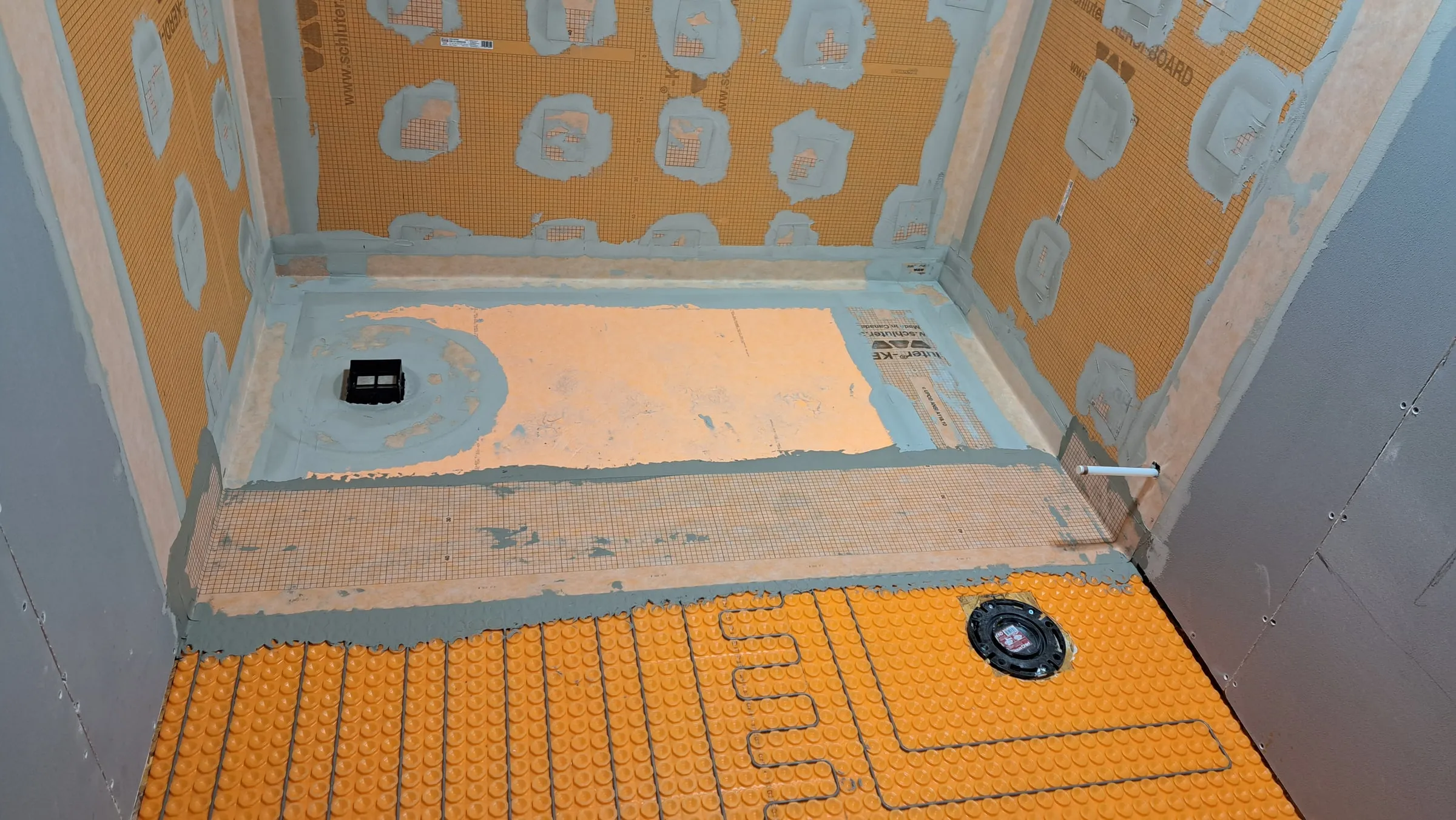 Shower pan with bonded waterproofing on the walls and an uncoupling mat around the drain, before tiling