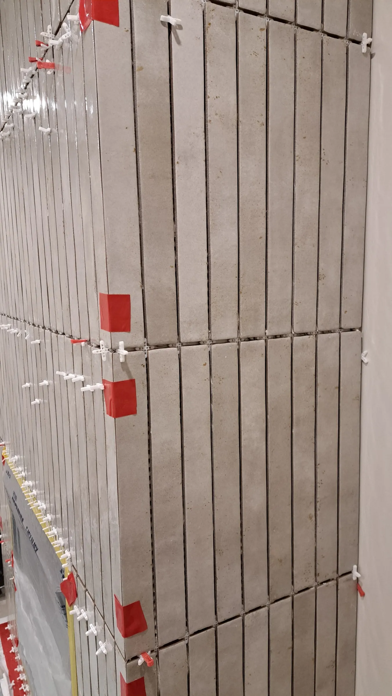 Wall tile held flat by levelling clips and wedges while the mortar sets
