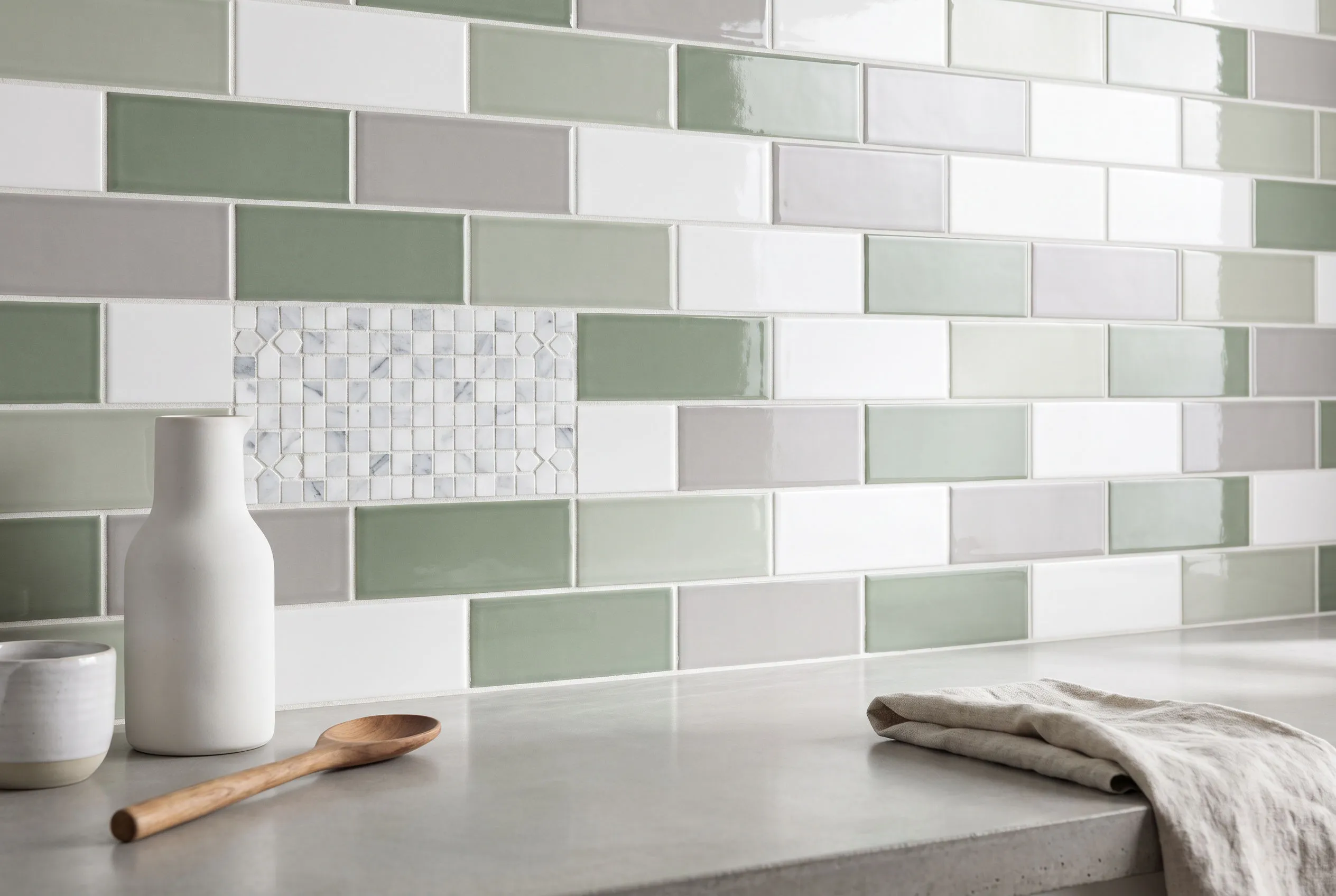 Glossy subway tiles in white, sage green and grey in a running-bond backsplash pattern with a small marble mosaic accent